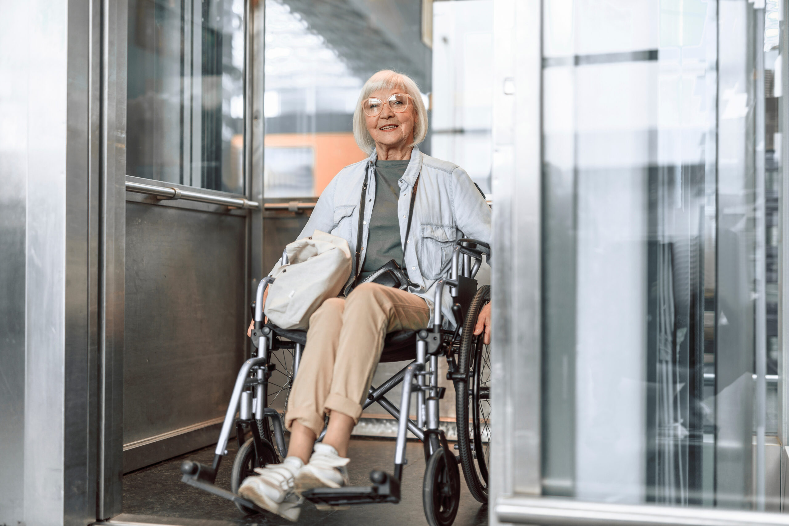 Mature lady in glasses on disabled carriage using elevator