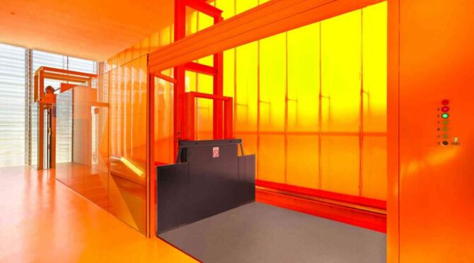 Interior space with vibrant orange walls, translucent yellow panels, and an industrial-style lift platform featuring a black gate.