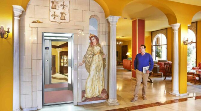 Man in hotel lobby near elevator with medieval-style mural.