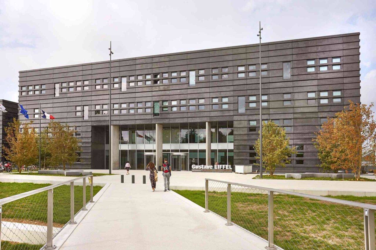 A modern building with a dark facade, multiple rows of windows, and glass doors at the central entrance.