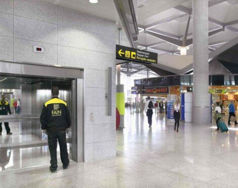 Airport interior with an elevator, signage, and people.