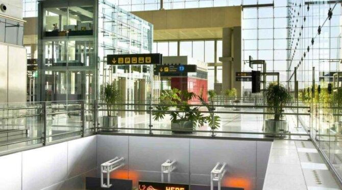 Airport terminal interior with escalators and glass windows.