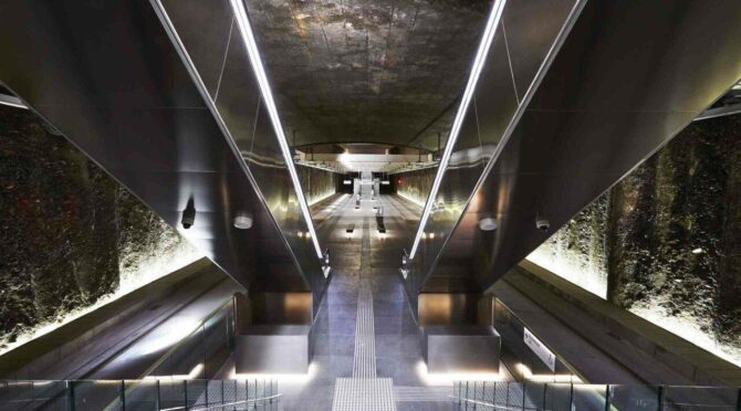 Underground train station with escalators, rocky walls, and sleek design elements.