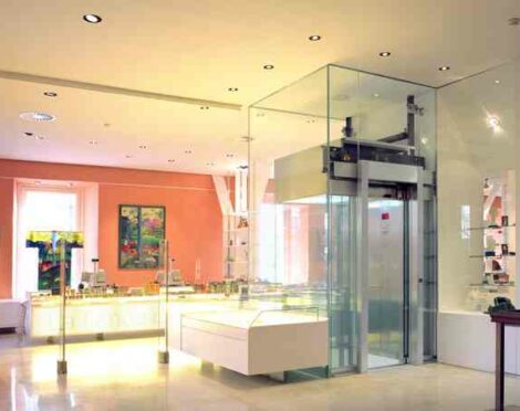Modern showroom interior with a glass elevator and warm-toned walls.